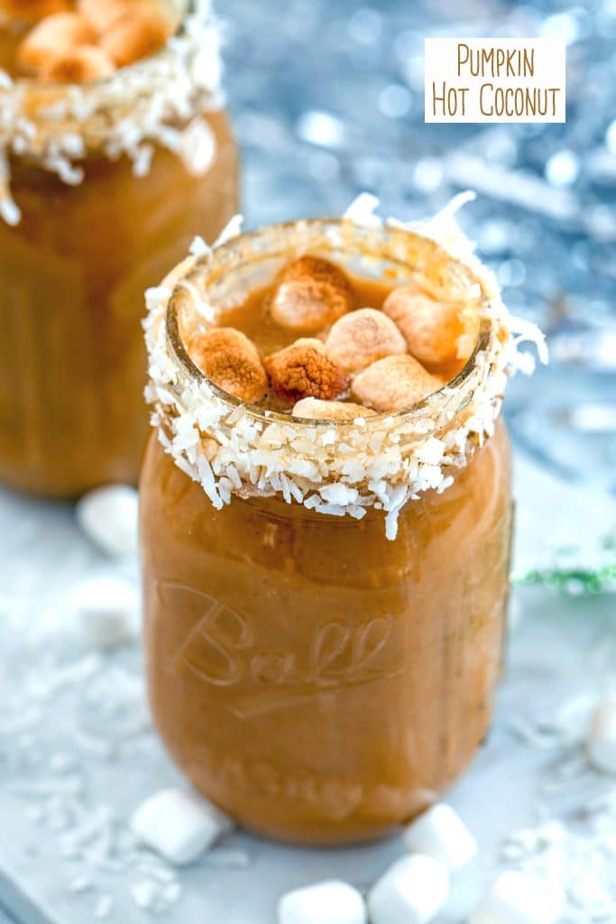Front view of a coconut-rimmed mason jar filled with pumpkin hot coconut drink with rum and topped with toasted marshmallows with a second drink in the background and recipe title at top