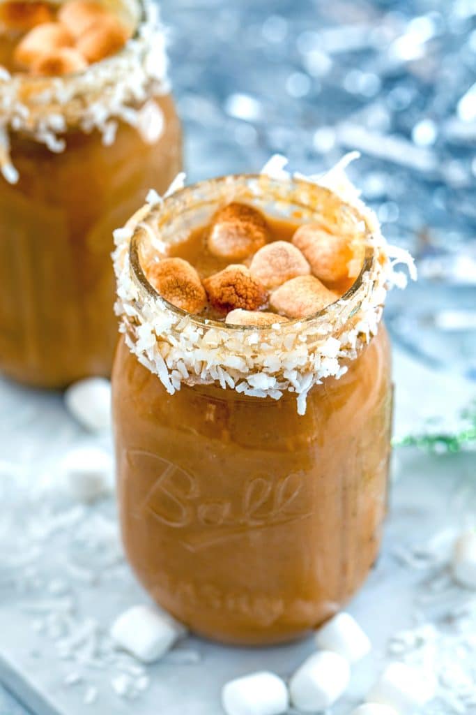 Front view of a coconut-rimmed mason jar filled with pumpkin hot coconut drink with rum and topped with toasted marshmallows with a second drink in the background