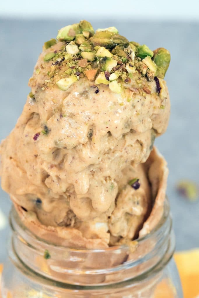 Close-up head-on view of pumpkin ice cream with pistachio swirl with lots of crushed pistachios on top in cone in mason jar