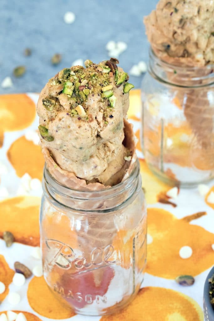 Head-on view of pumpkin ice cream with pistachio swirl in a cone set in a mason jar with a second cone in the background