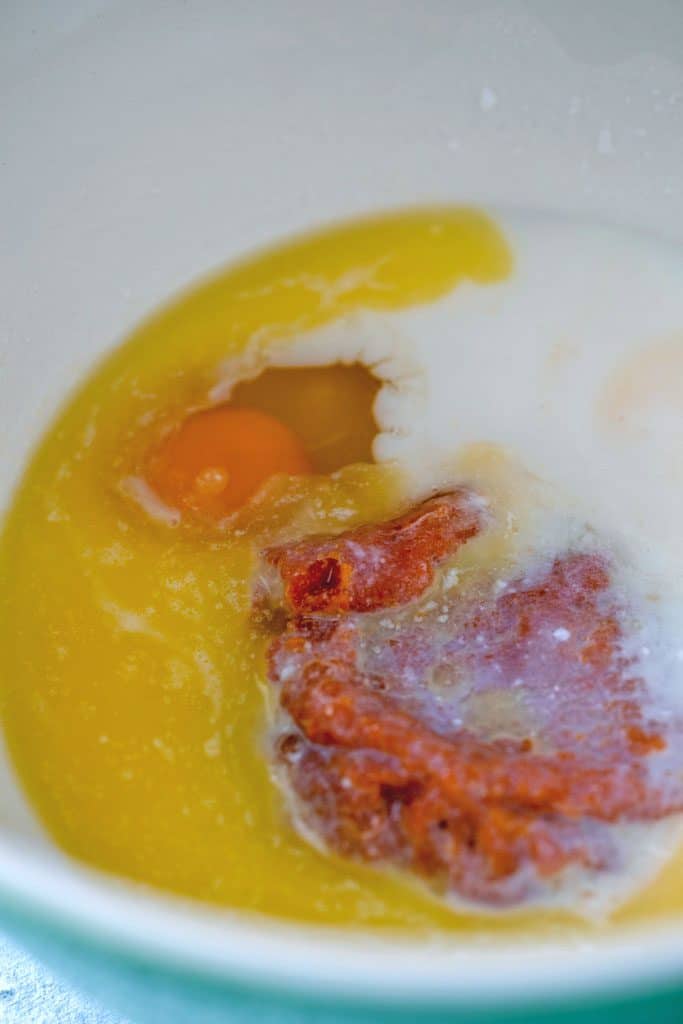 A bowl filled with wet ingredients for pumpkin pancakes, including butter, pumpkin puree, buttermilk, and egg