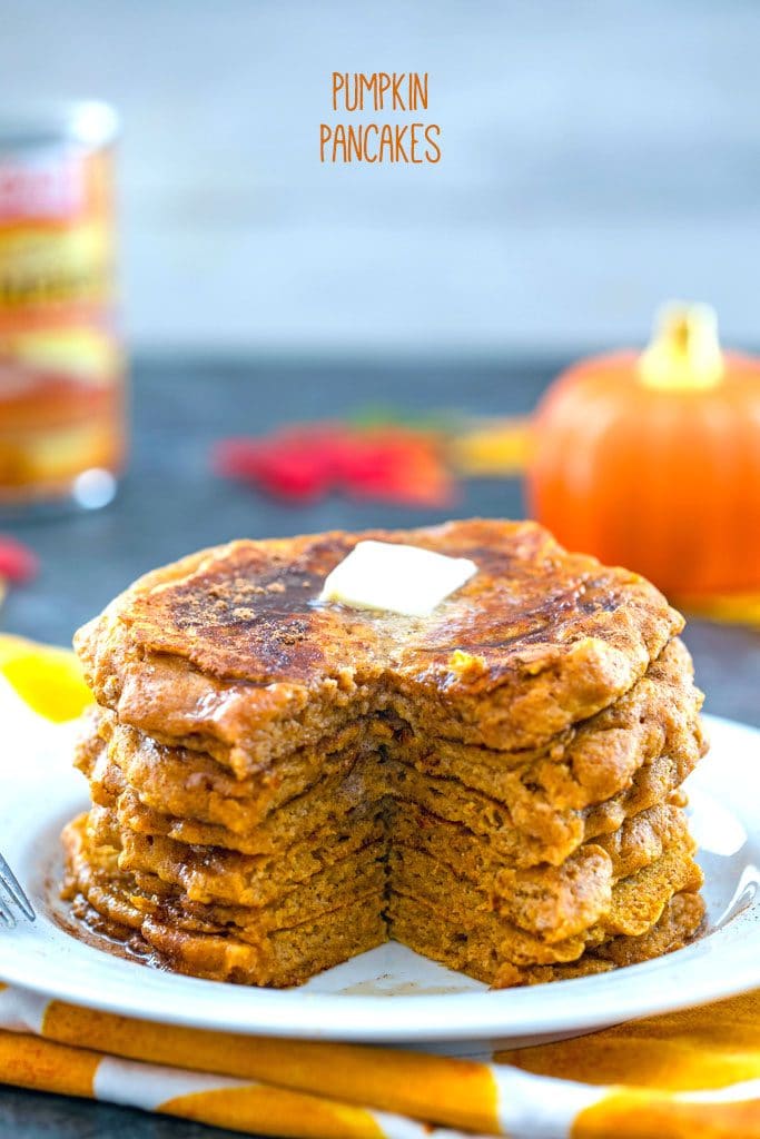 Head-on view of white plate with stack of pumpkin pancakes with with a wedge cut out and a pat of butter on top with "Pumpkin Pancakes" text at top