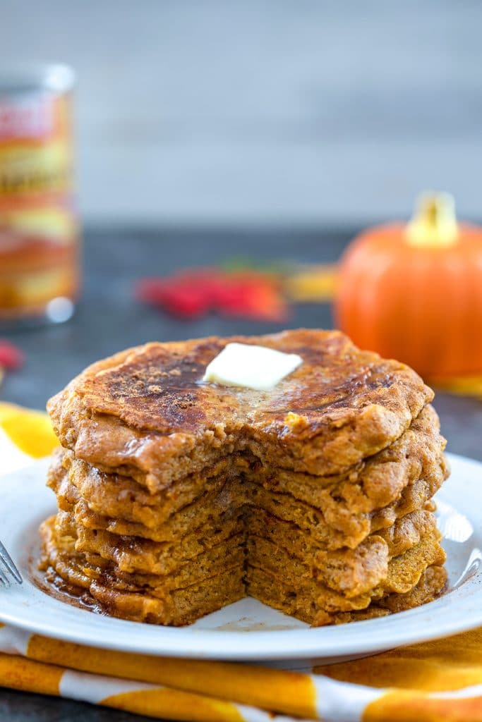 Head-on view of white plate with stack of pumpkin pancakes with with a wedge cut out and a pat of butter on top