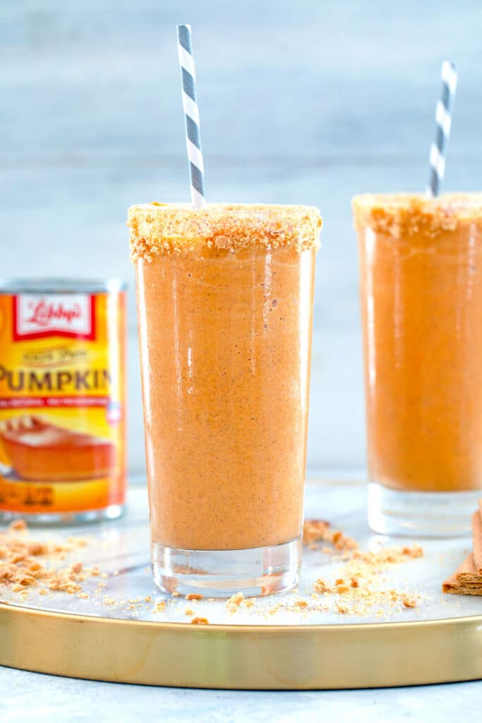 Head-on view of two pumpkin pie milkshakes on marble tray with can of pumpkin and graham cracker crumbs in the background