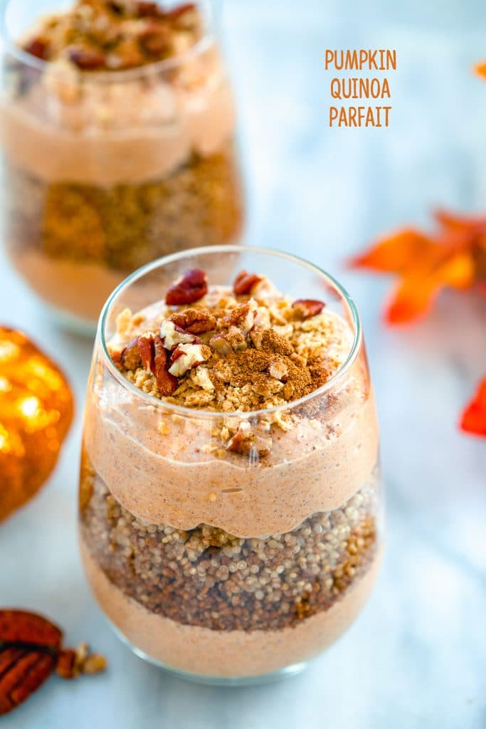 Overhead view of a pumpkin quinoa parfait in a glass with layers of pumpkin yogurt and quinoa with a second parfait and fall leaves in the background and recipe title at the top