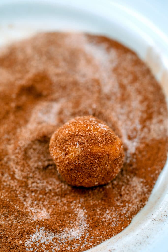 Pumpkin snickerdoodle balls on a plate being rolled in cinnamon sugar