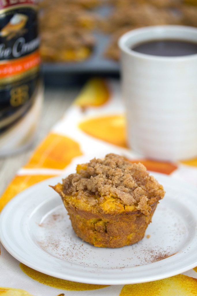 Head-on closeup view of a pumpkin spice french toast muffin on a white plate with cup of coffee in the background