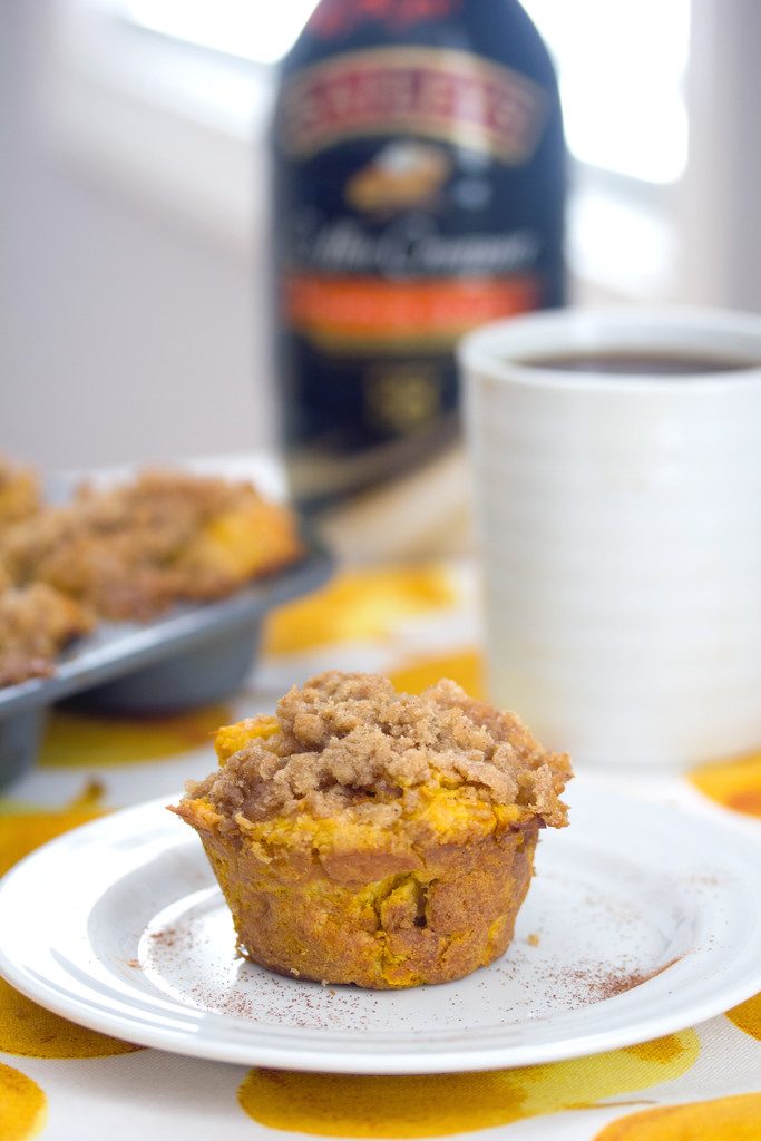 Head-on view of a pumpkin spice french toast muffin on a white plate with muffin tin, cup of coffee, and bottle of coffee creamer in background