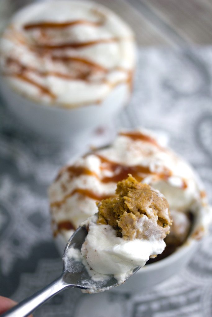 Close-up of a spoon full of pumpkin mug cake being held over the mug with the rest of the cake and a second mug cake in the background