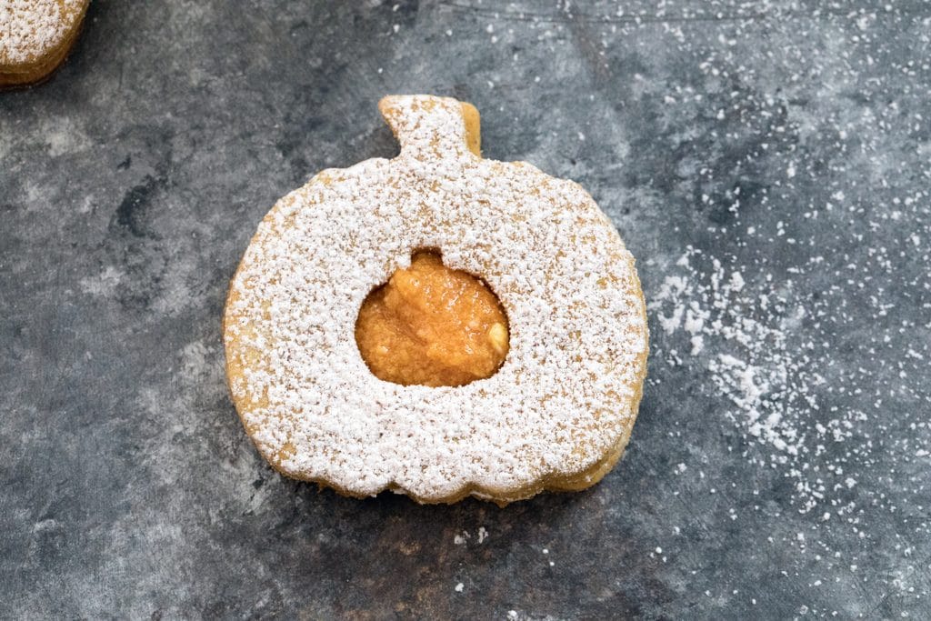 Landscape overhead closeup view of a pumpkin spice linzer cookie with confectioners' sugar and pumpkin filling on a dark surface