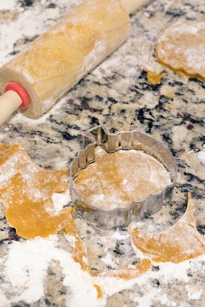Overhead view of cookie dough on counter with pumpkin shaped cookie cutter and mini rolling pin