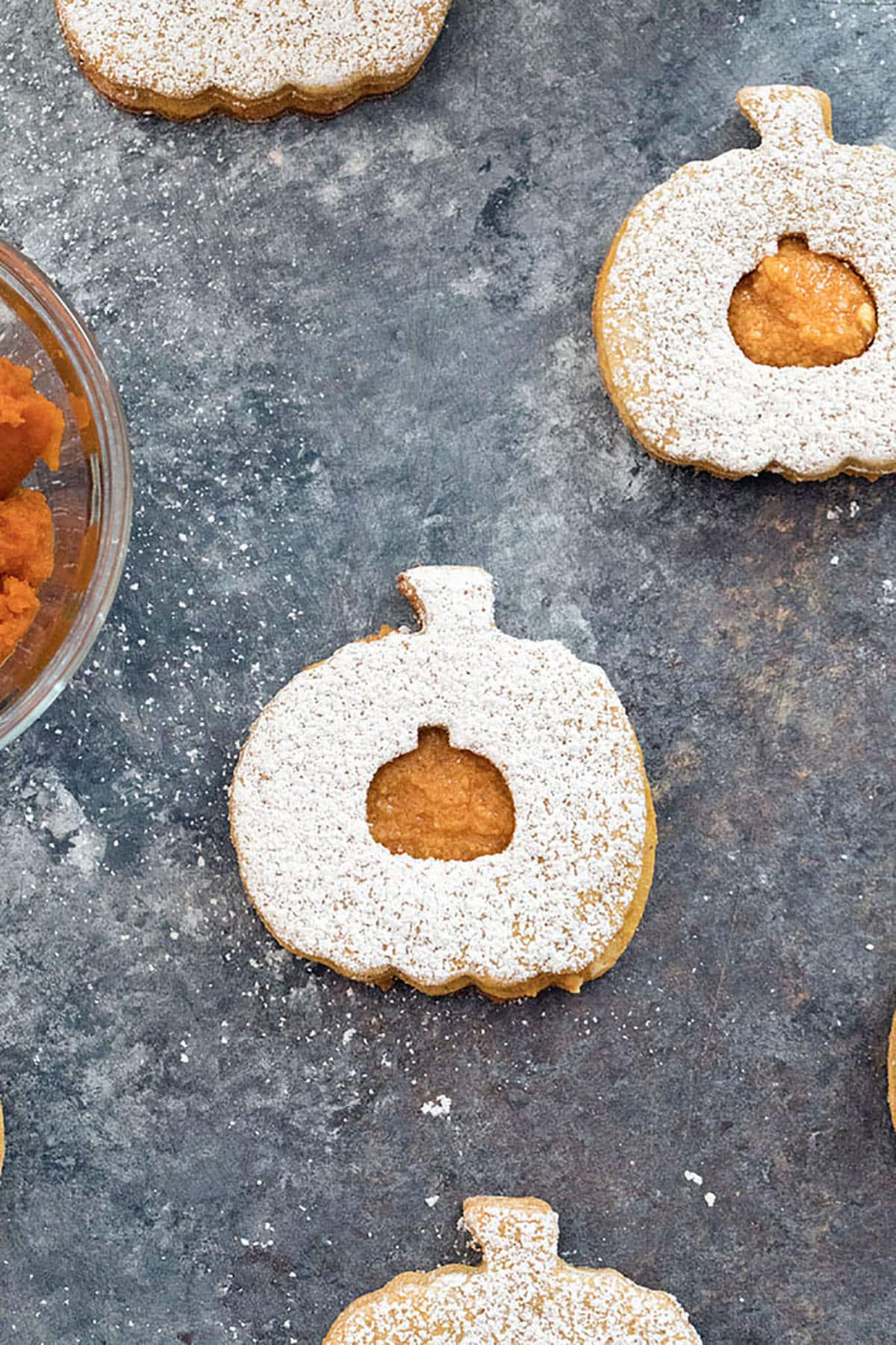 Overhead view of multiple pumpkin spice linzer cookies topped with confectioners' sugar on a dark background.
