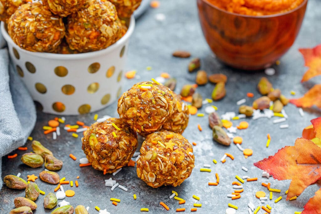 Landscape view of pumpkin spice energy balls with more energy bites and pumpkin puree in background with ingredients and fall leaves all around
