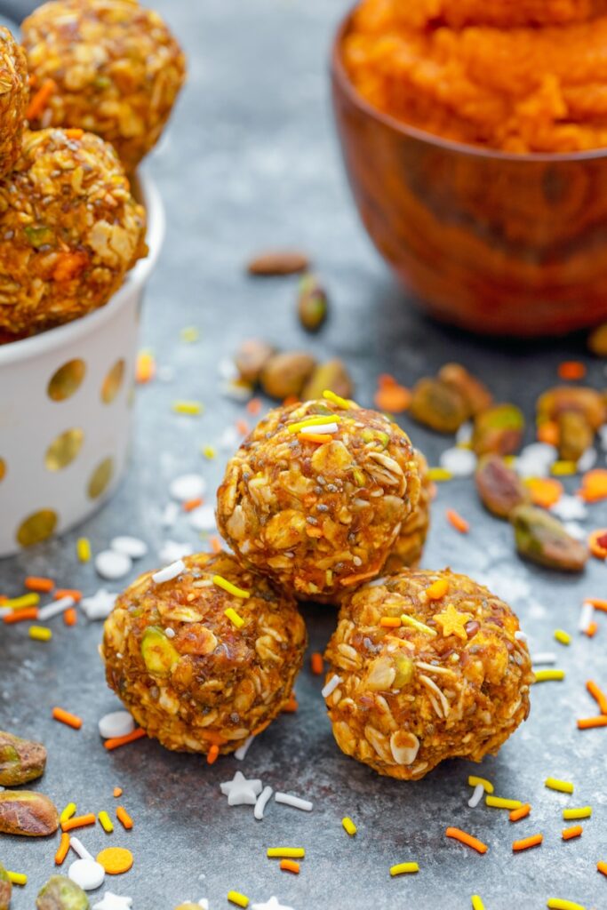Head-on closeup view of pumpkin spice pistachio energy balls with pumpkin puree and more energy bites in background with ingredients all around