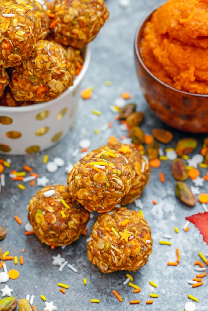 Overhead view of pumpkin spice pistachio energy balls with more energy bites and pumpkin puree in background and ingredients all around