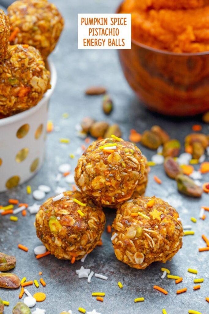 Head-on closeup view of pumpkin spice pistachio energy balls with pumpkin puree and more energy bites in background with ingredients all around and recipe title at top