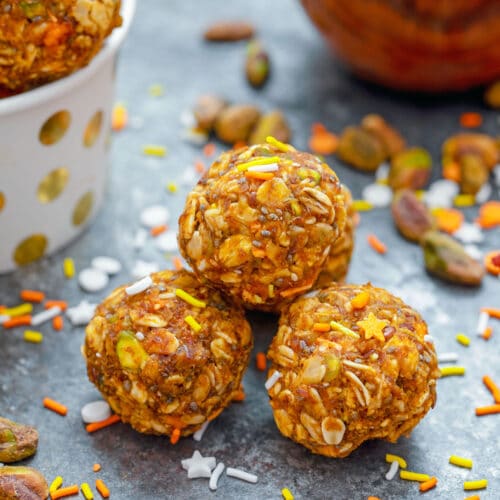 Head-on closeup view of pumpkin spice pistachio energy balls with pumpkin puree and more energy bites in background with ingredients all around
