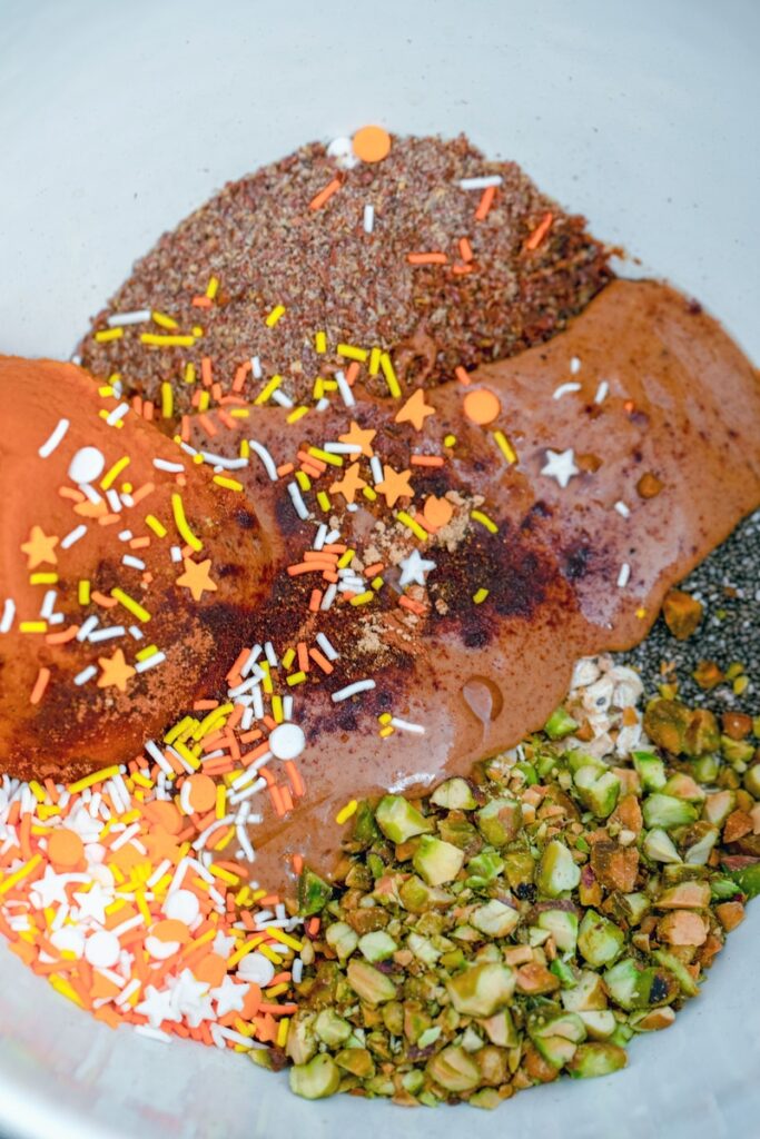 Mixing bowl with pumpkin puree, almond butter, oats, pistachios, flaxseed, chia seeds, spices, and sprinkles.