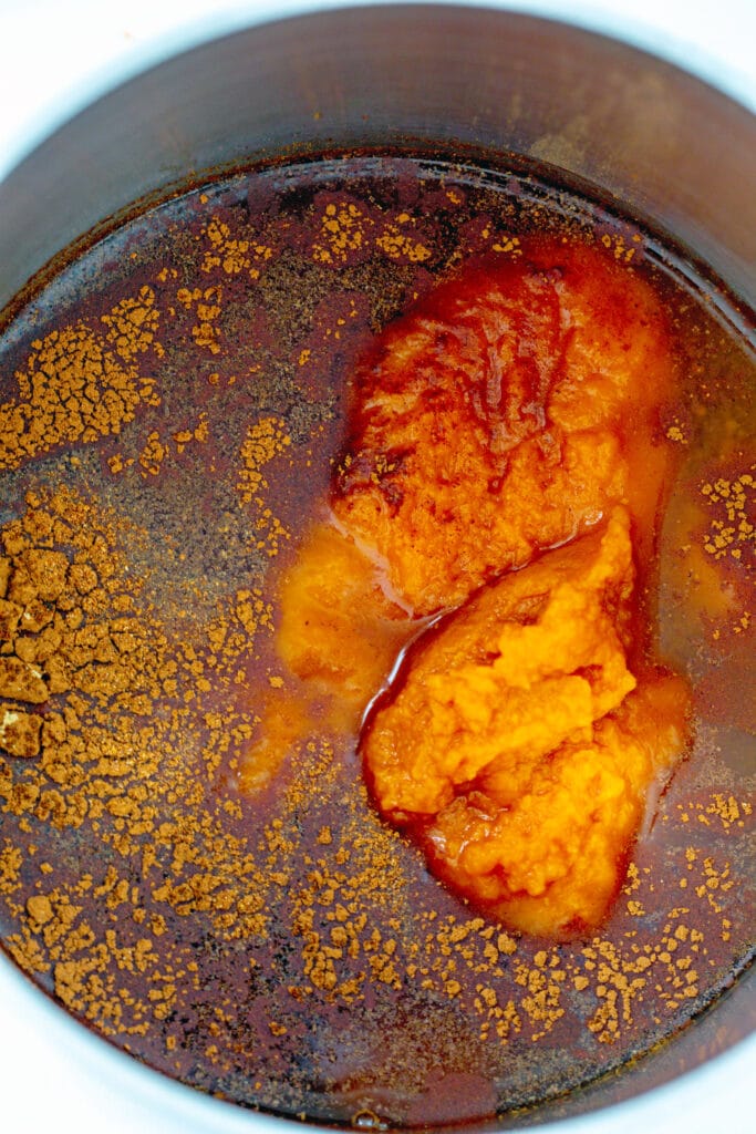 Water and sugar with cinnamon, nutmeg, ginger, and pumpkin puree in saucepan