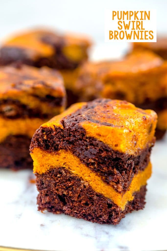 Head-on closeup view of a pumpkin swirl brownie with pumpkin and chocolate layers with more brownies in the background and recipe title at top of image