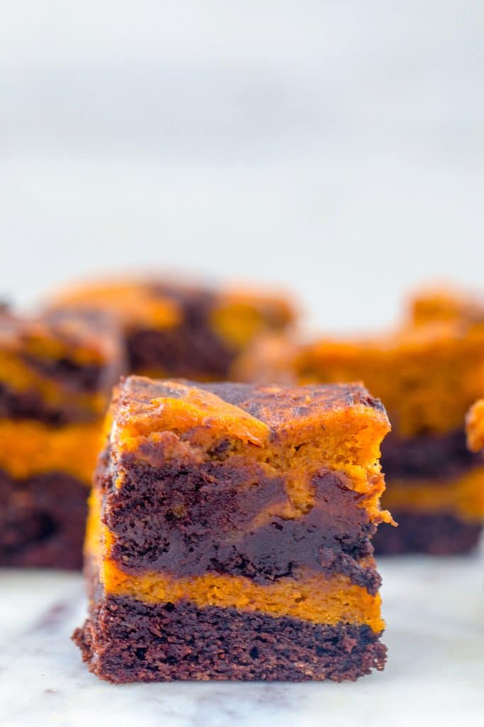 Head-on closeup view of a pumpkin swirl brownie on a marble surface with more brownies in the background