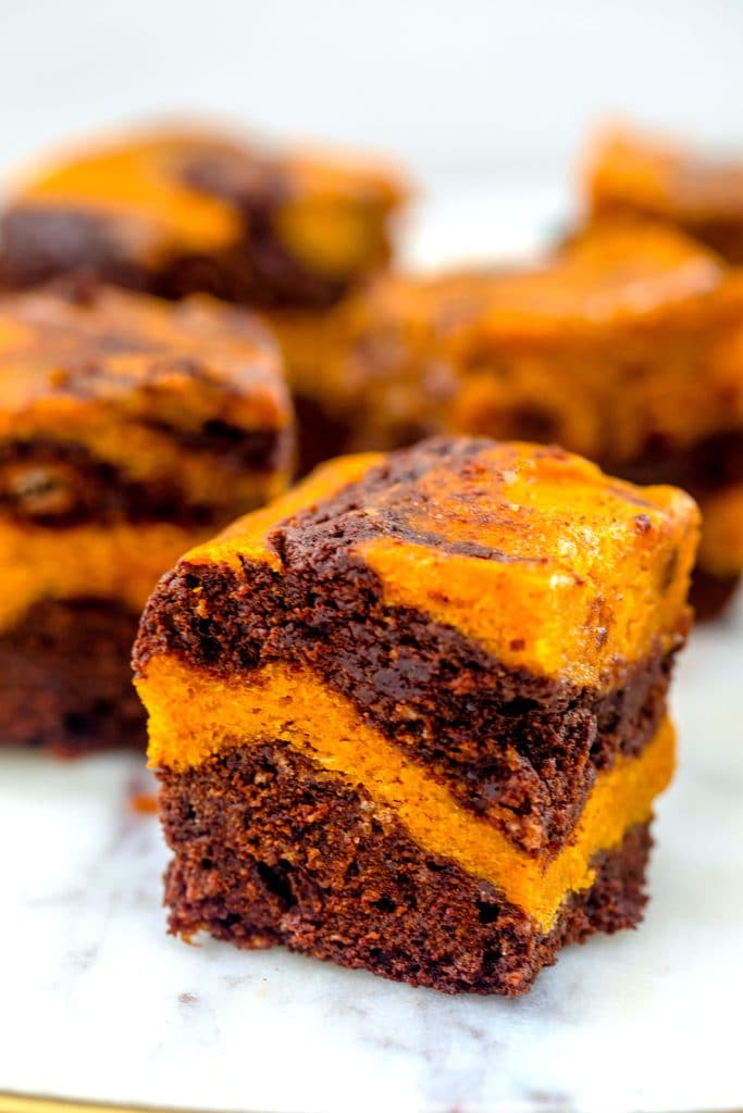 Head-on closeup view of a pumpkin swirl brownie with pumpkin and chocolate layers with more brownies in the background