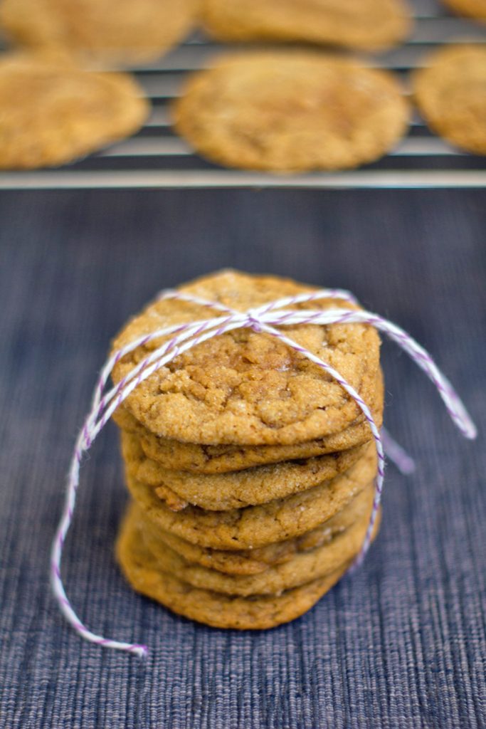 Head-on view of a stack of pumpkin toffee gingersnap cookies tied up with baker's twine with a baking rack with more cookies in the background