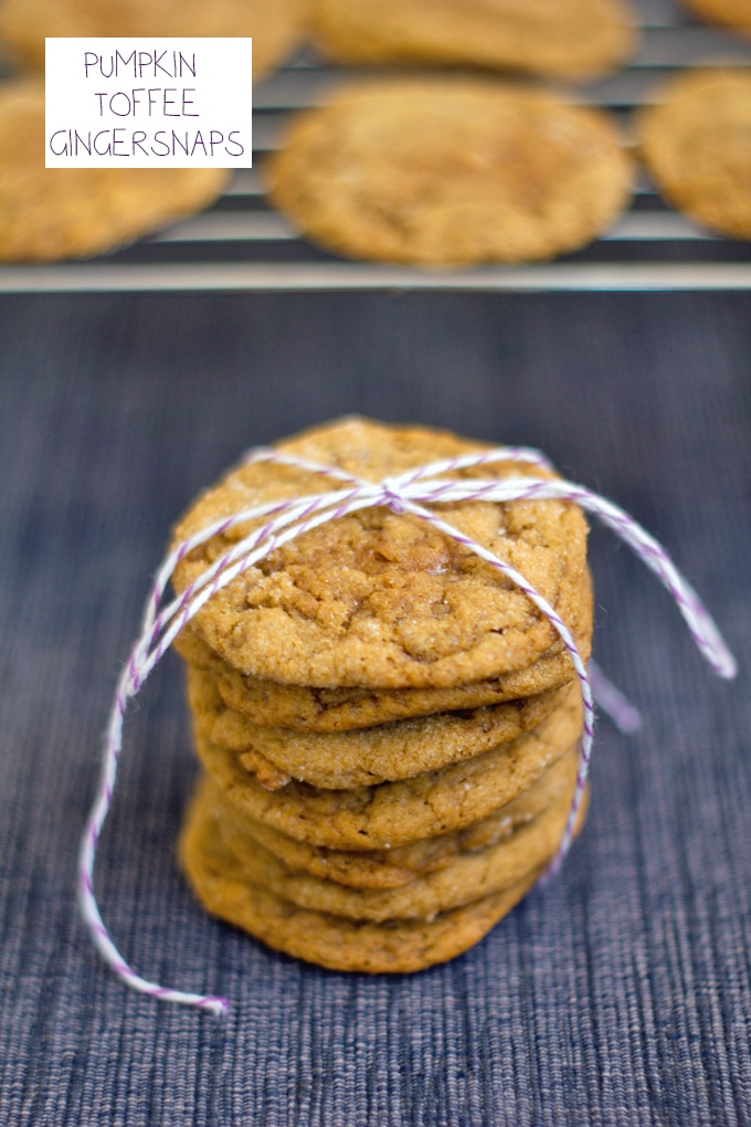 Head-on view of a stack of pumpkin toffee gingersnap cookies tied up with baker's twine with a baking rack with more cookies in the background and recipe title at top