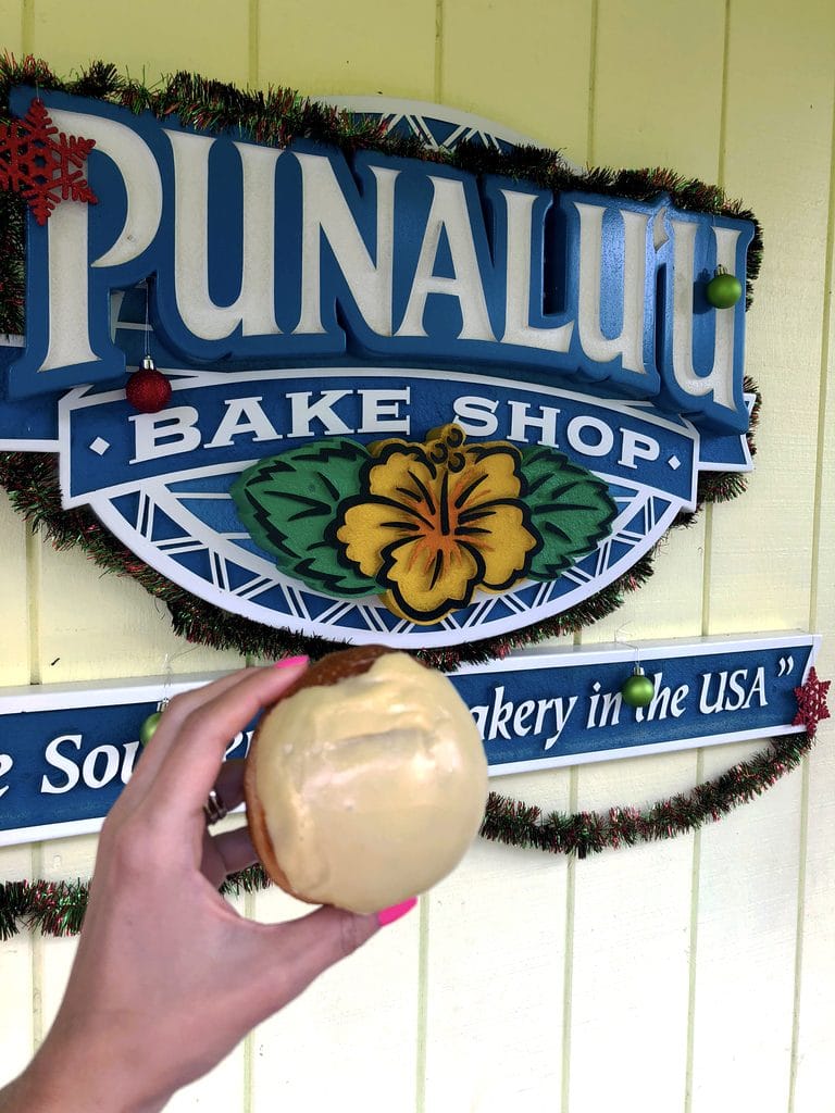 Passionfruit malasada in front of Punalu'u Bake Shop sign, the southernmost bakery in the United States on the Big Island of Hawaii