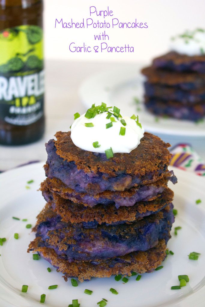 Head-on view of a stack of purple mashed potato pancakes with garlic and pancetta topped with Greek yogurt and chives with a bottle of beer and more potato pancakes in the background and recipe title at top