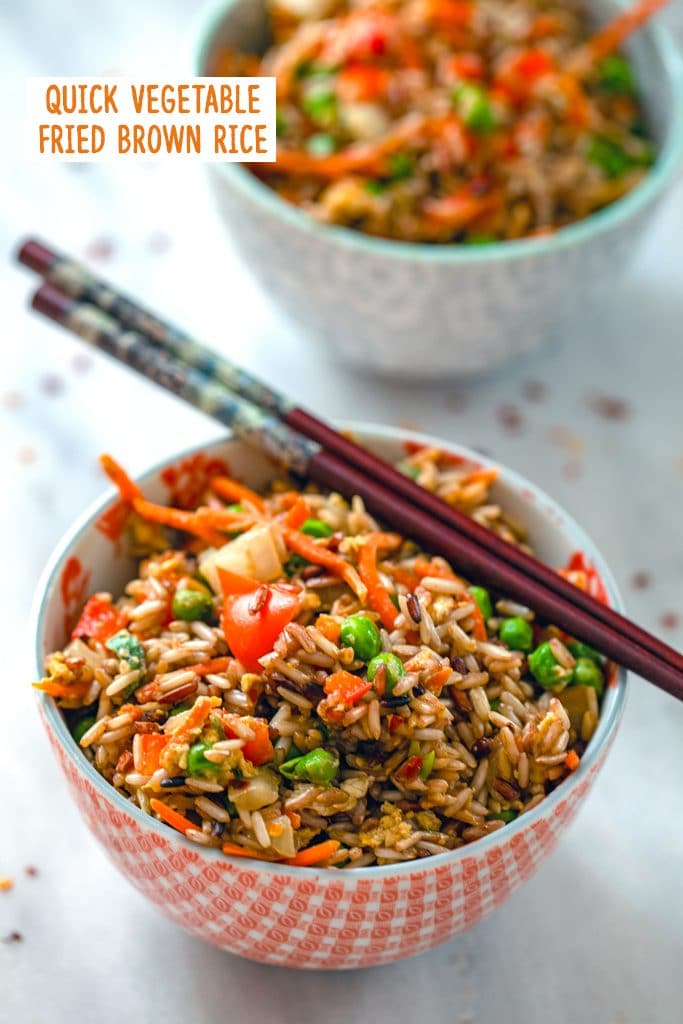 Head-on view of a bowl of quick vegetable fried brown rice with chopsticks balancing on it, a second bowl of rice in the background, and "Quick Vegetable Fried Brown Rice" text at the top