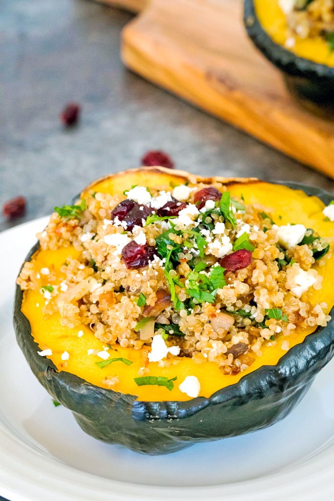 Head-on view from the side of a half an acorn squash stuffed with quinoa, mushrooms, spinach, dried cranberries, and feta