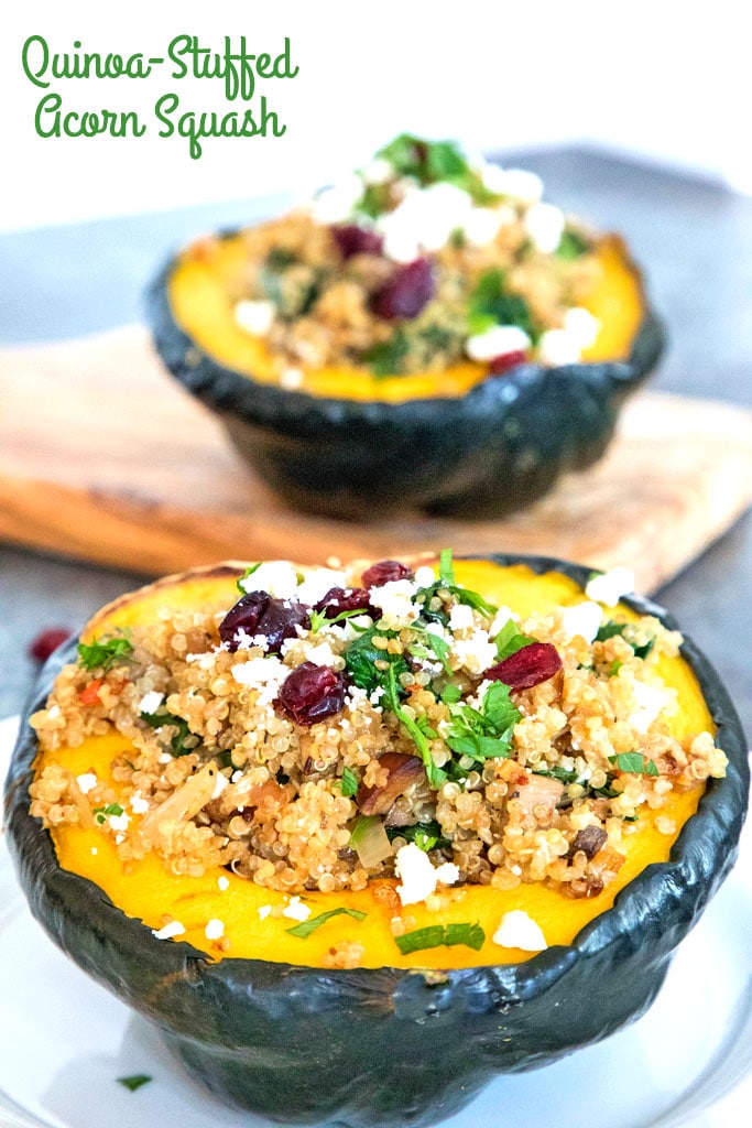 Head-on view of an acorn squash half overflowing with quinoa, spinach, feta, and dried cranberries with a second squash half on a cutting board in the background and recipe title at top