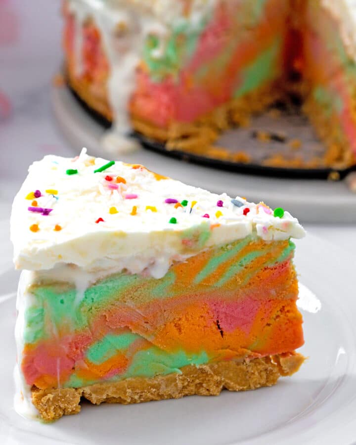 Head-on view of a slice of rainbow sherbet cake with rest of cake in background