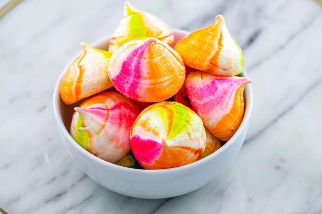 Overhead view of a bowl of pink, green, and orange rainbow sherbet meringues.