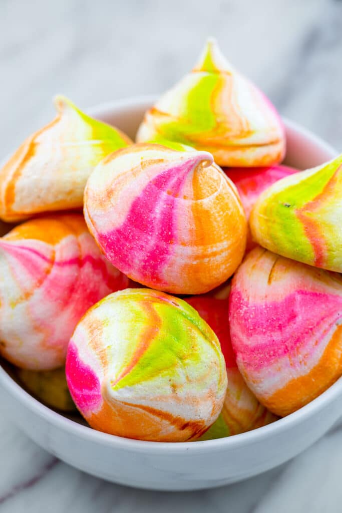 Head-on view of a white bowl filled with pink, orange, and green rainbow sherbet meringues.