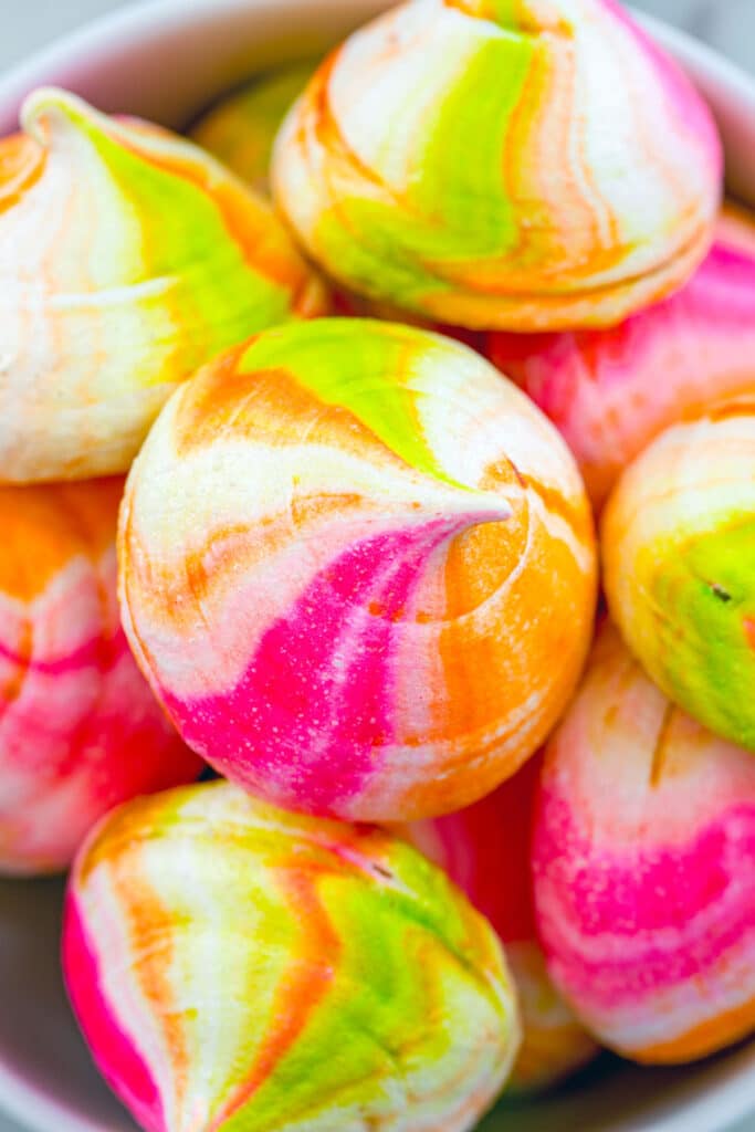 Overhead view of a bowl of pink, green, and orange rainbow sherbet meringues.