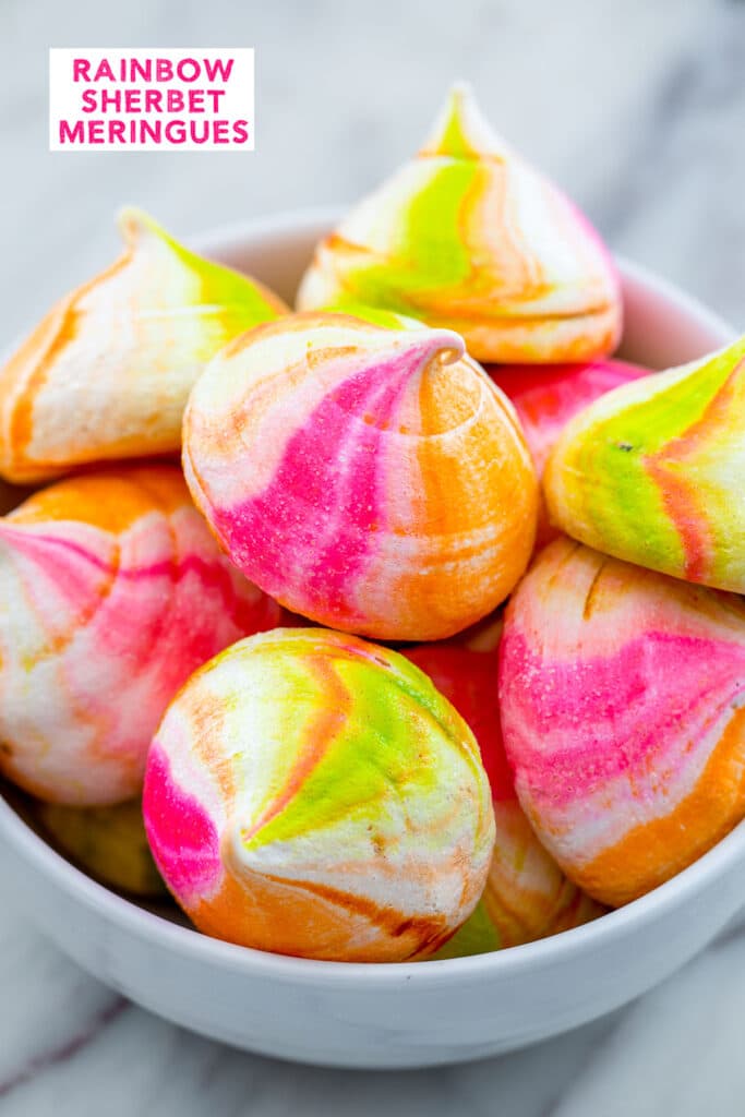 Head-on view of a white bowl filled with pink, orange, and green rainbow sherbet meringues with recipe title at top.