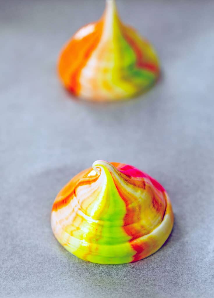 View of two meringues piped onto parchment paper ready to be baked.