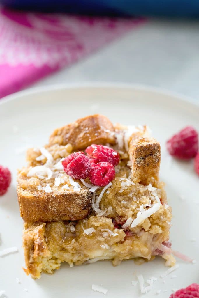 A closeup of a serving of raspberry coconut french toast casserole topped with shredded coconut and fresh raspberries