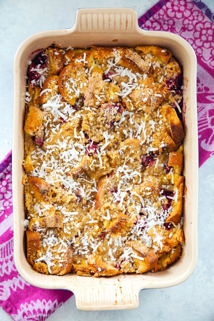 a bird's eye view of the raspberry coconut french toast casserole in the baking dish just out of the oven with a browned crispy top and on a pink dishtowel