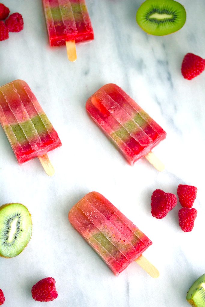 Overhead view of four raspberry kiwi sangria popsicles on a marble surface with raspberries and kiwi halves