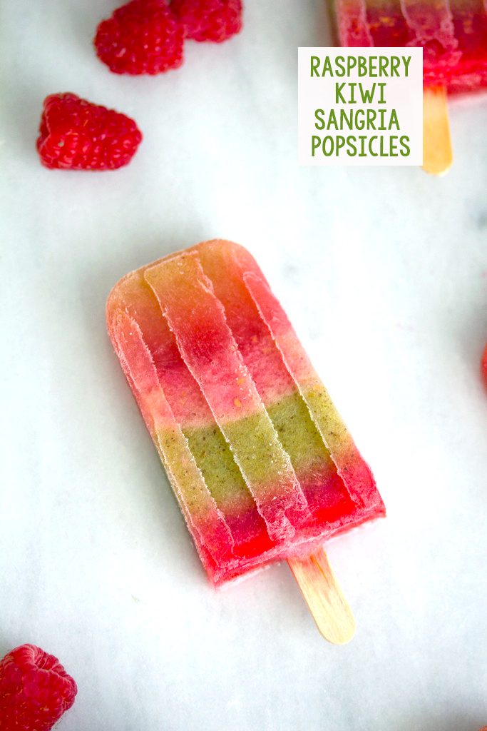 Overhead view of a raspberry kiwi sangria popsicle on a marble surface surrounded by raspberries with recipe title at top