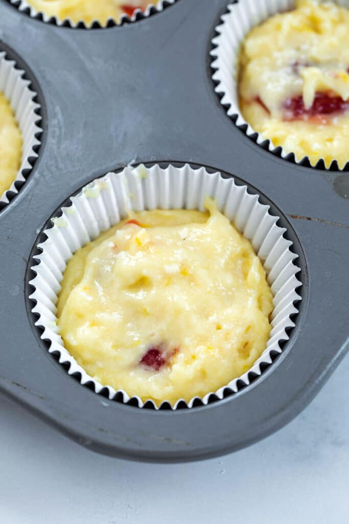 Lemon cupcake batter covering raspberry jam in cupcake tin