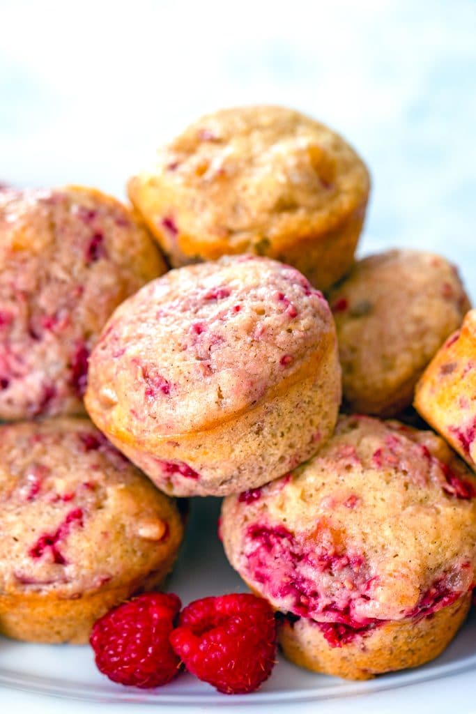 Head-on view of a plate full of raspberry, mango, ginger muffins piled up with fresh raspberries on the side
