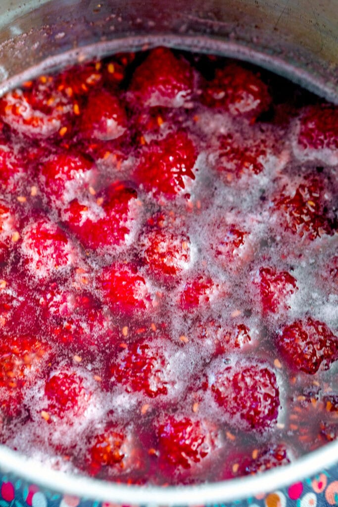 Overhead view of raspberries simmering in saucepan with sugar and water