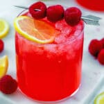 Head-on closeup view of a raspberry vodka lemonade with lemon slice and fresh raspberries.