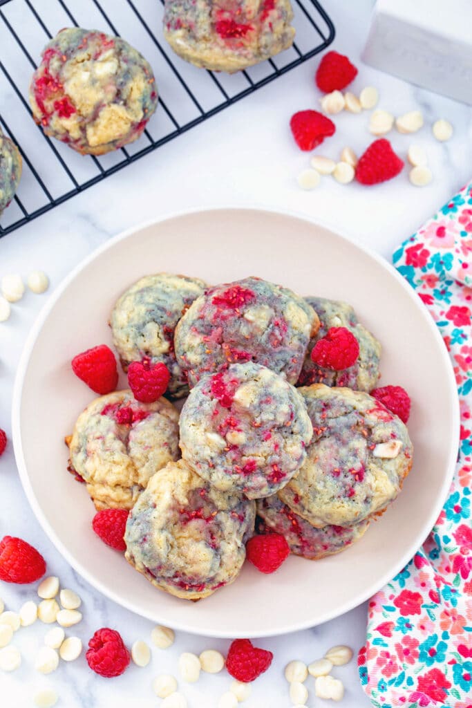Bird's eye view of raspberry white chocolate cookies on a plate with raspberries and white chocolate all around.