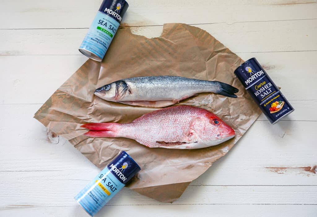 Overhead view of whole branzino and whole red snapper on parchment paper with Morton Salt containers.