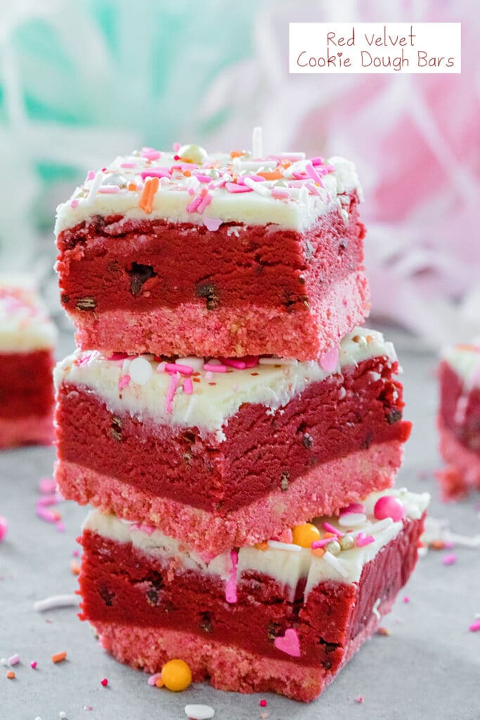 Head-on view of a stack of three red velvet cookie dough bars with white chocolate ganache topping and Valentine's Day sprinkles with sprinkles all around and recipe title at top.